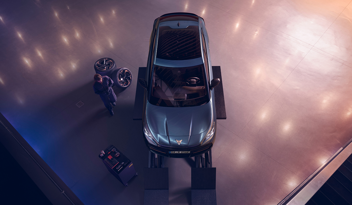 Draufsicht auf einen CUPRA Tavascan in einer Werkstatt, neben dem Fahrzeug ein Mechaniker und abmontierte Räder